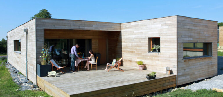 Maison de plein pied en bois, avec un encreux format la terrasse. Le bardage bois vertical est naturel.