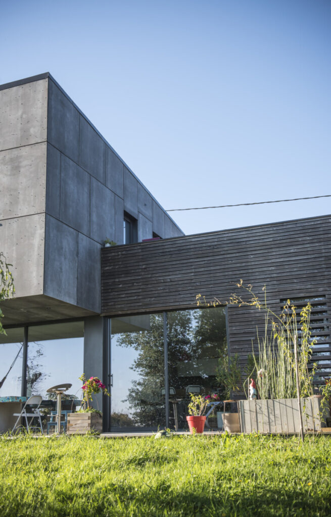 Maison contemporaine en bois et parement béton, jardin enherbé.