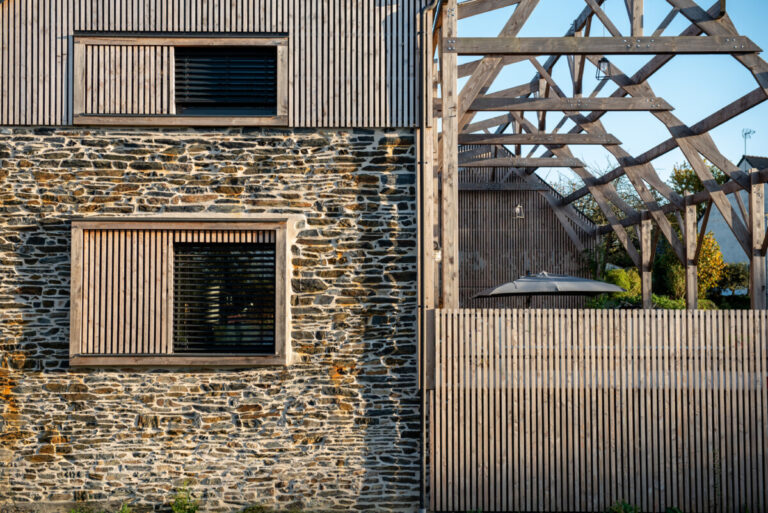 Photo de détail de liaison entre le bâtiment existant pierres réhabilité et la pergola bois adjacente.