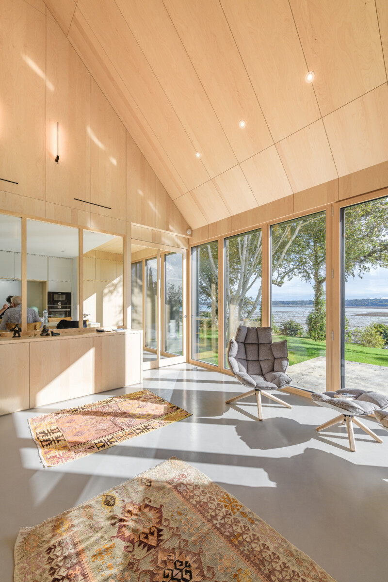 Intérieur de la maison passive, en bois clair et chaleureux, avec une grande baie vitrée offrant une belle vue sur la mer 