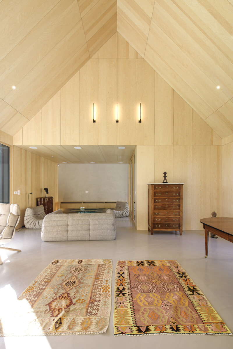 Vue de face du pignon Intérieur de la maison passive, en bois clair et chaleureux. Le salon dispose de grands tapis de couleurs chaudes, les meubles sont design 